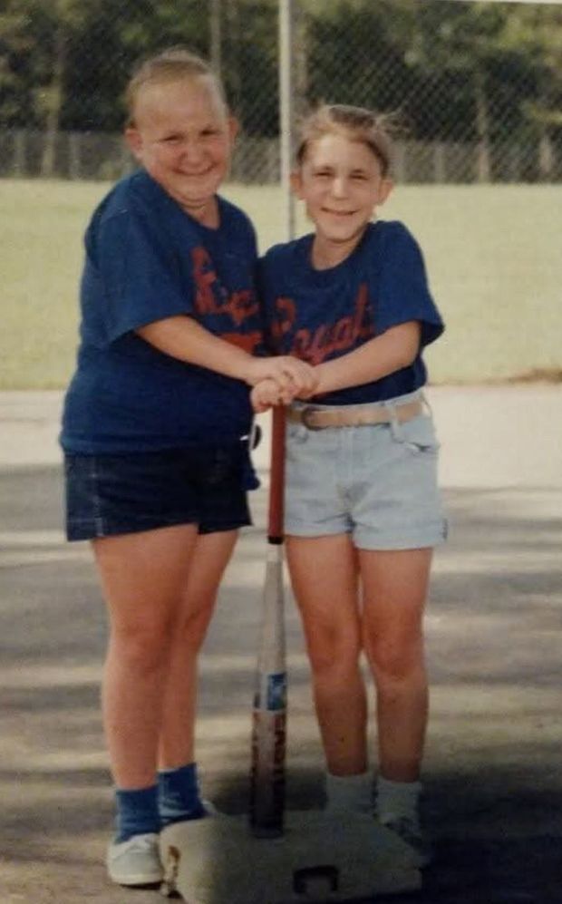 An old print of two young players in navy shirts standing on the pavement with their hands stacked on the same bat