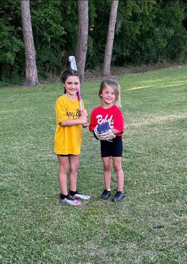 Two girls in different team shirts standing together holding a glove