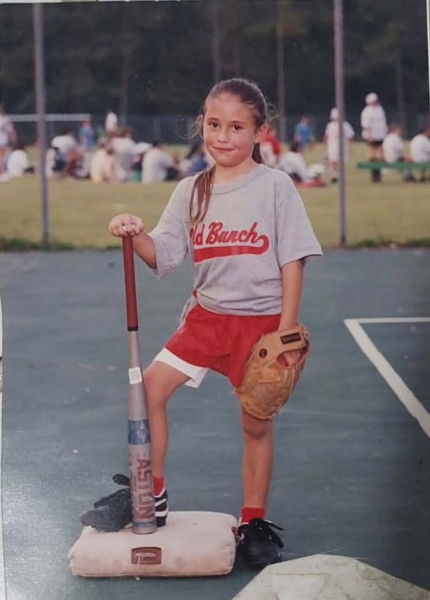 An old print of a girl in a Wild Bunch shirt posing with her foot on a base and a glove on her knee