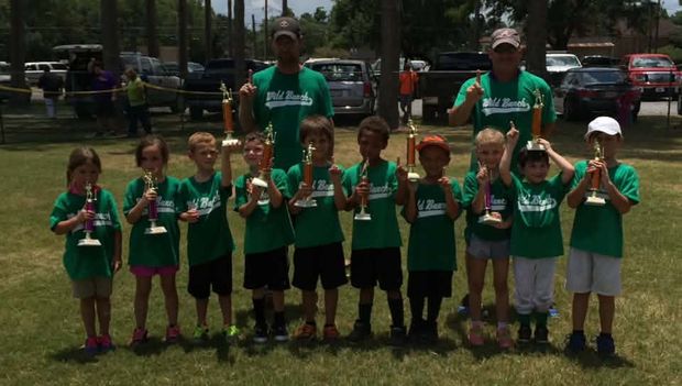 A team of children in green Wild Bunch shirts standing on the grass holding trophies
