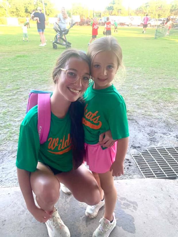 A teenager and a young girl in matching green Wildcats shirts crouched together
