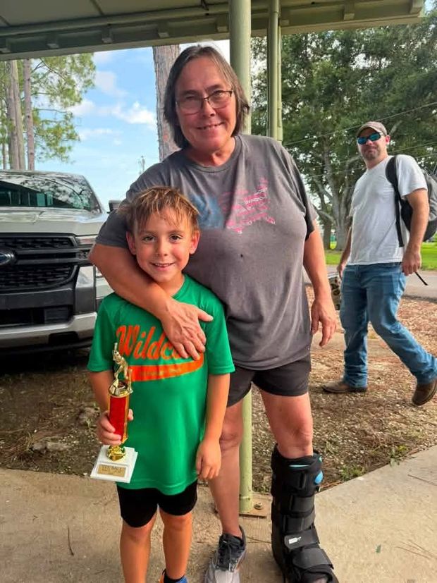 An older woman with her arm around a boy in a green Wildcats shirt holding a trophy