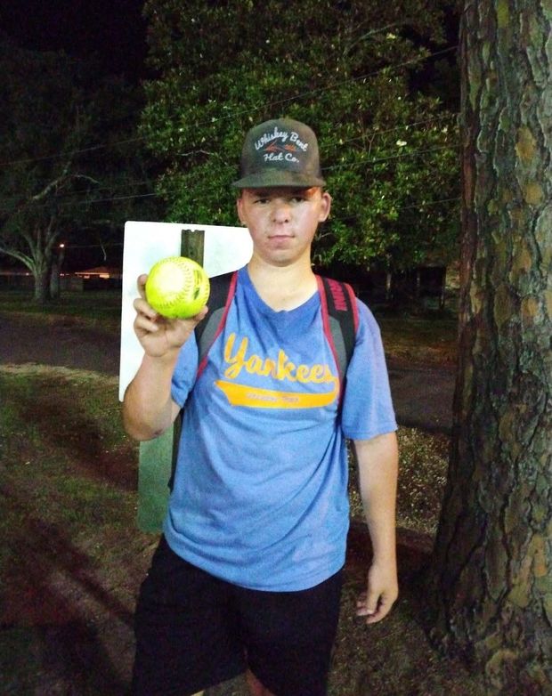A teenager in a blue Yankees shirt holding up a softball at night