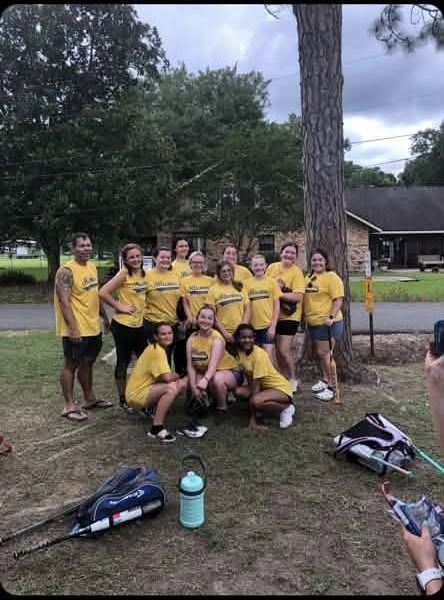 A team in yellow shirts posed together beside a pine tree